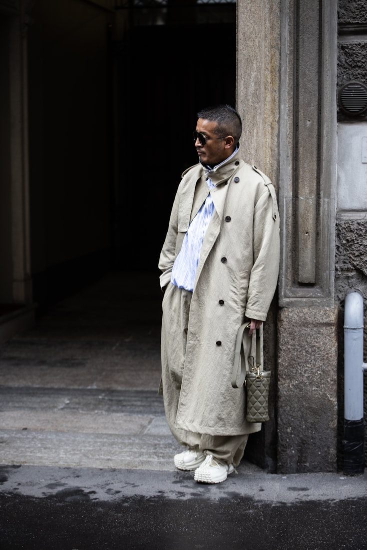 A man in a long stone-coloured trench coat in a doorway